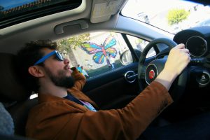 Portrait of Joshua Alexander driving, with colorful butterfly mural in background